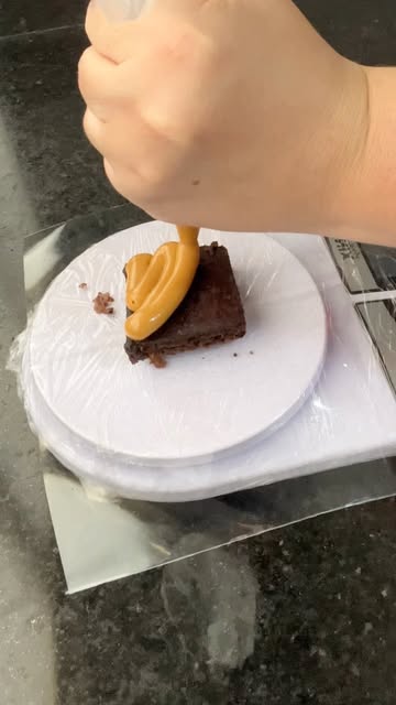 Mão cobrindo um brownie com doce de leite usando um bico de confeitar